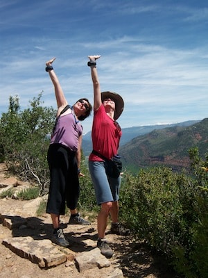 Two hikers on a dirt trail arms outstretched